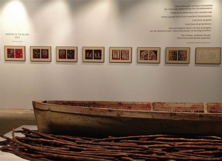 Foreground: part of THEIR SPIRITS GONE BEFORE THEM, 2006, cottonwood canoe, dried sugar cane. Background: WEEPING IN THE BLOOD prints with Paul Ferrini poem